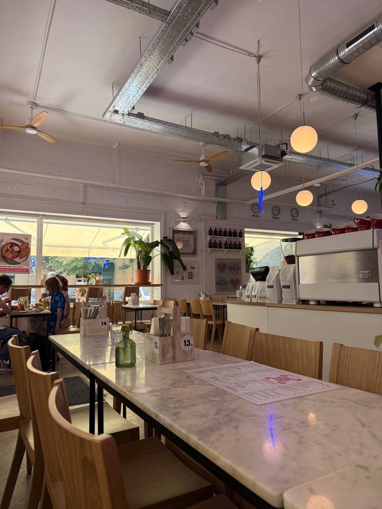 Интерьер Babka Deli — мраморные столы, деревянные стулья и кофемашина у окна